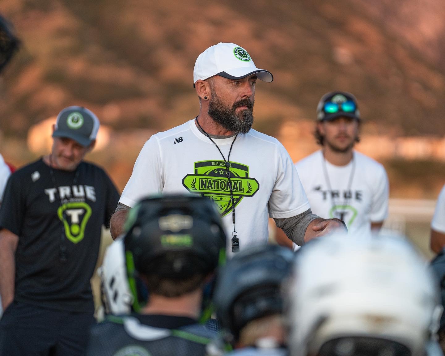 PJ Martin coaching on the field, speaking to players gathered around him at dusk
