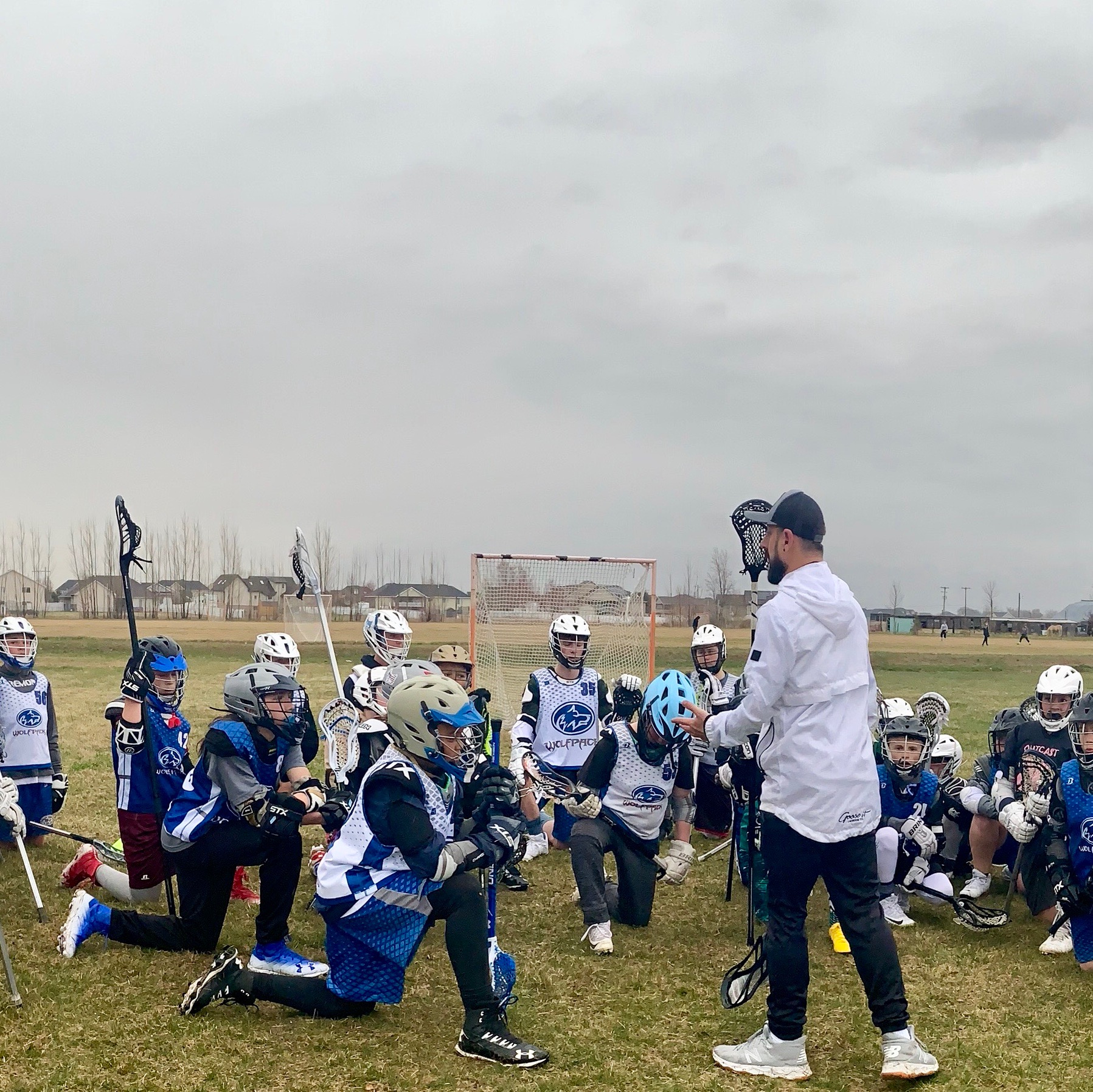 A coach leading a free community clinic for a kneeling group of youth players on an open grass field