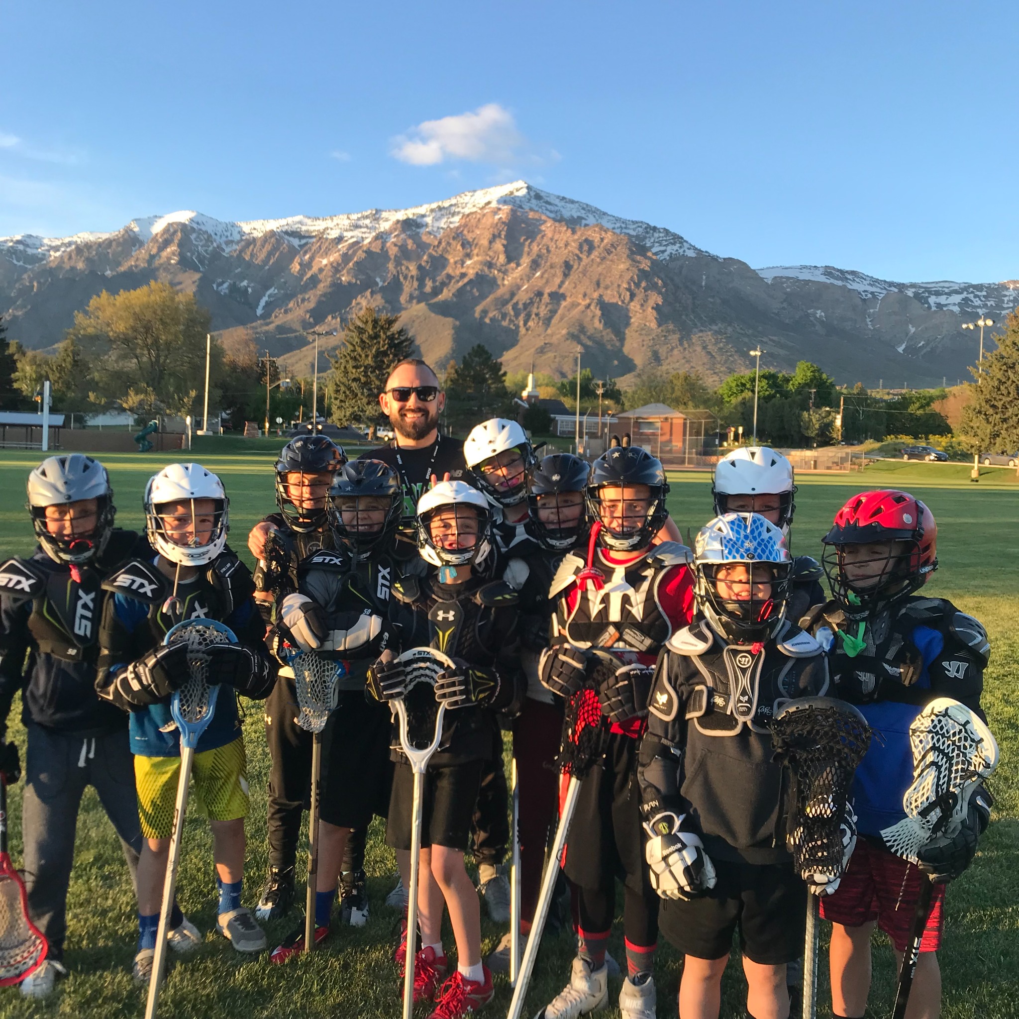 A youth lacrosse team and their coach posing together after practice with a mountain ridge behind them