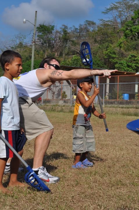 PJ Martin teaching a young player how to hold and pass with a lacrosse stick during a service trip in Costa Rica