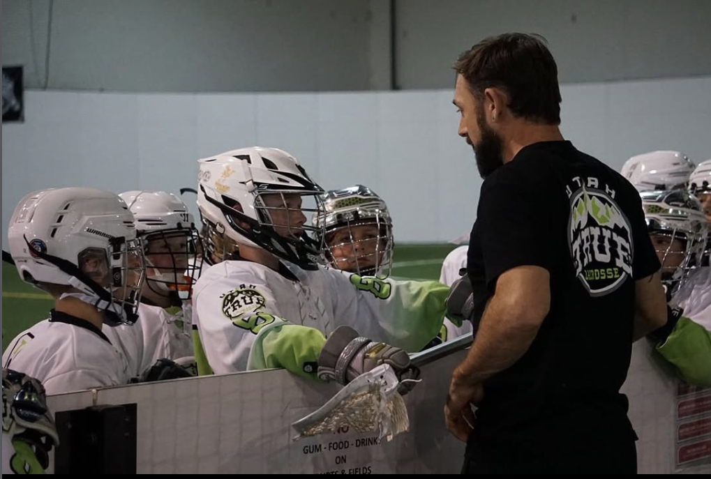 A coach giving instruction to players along the bench boards during indoor box lacrosse